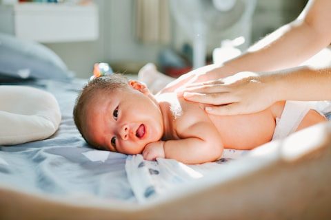 Baby liegt entspannt auf dem Rücken, während zwei Hände seinen Bauch massieren