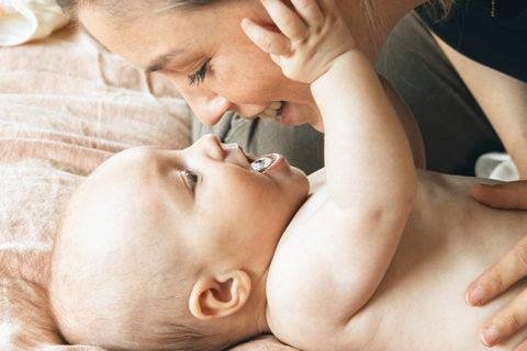 Mutter beugt sich lachend über ihr Baby, das ihr Gesicht berührt