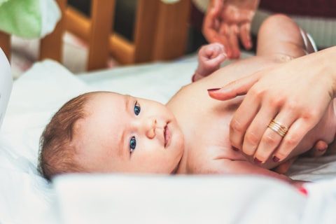 Baby liegt entspannt auf einer weißen Decke, während Hände es sanft massieren